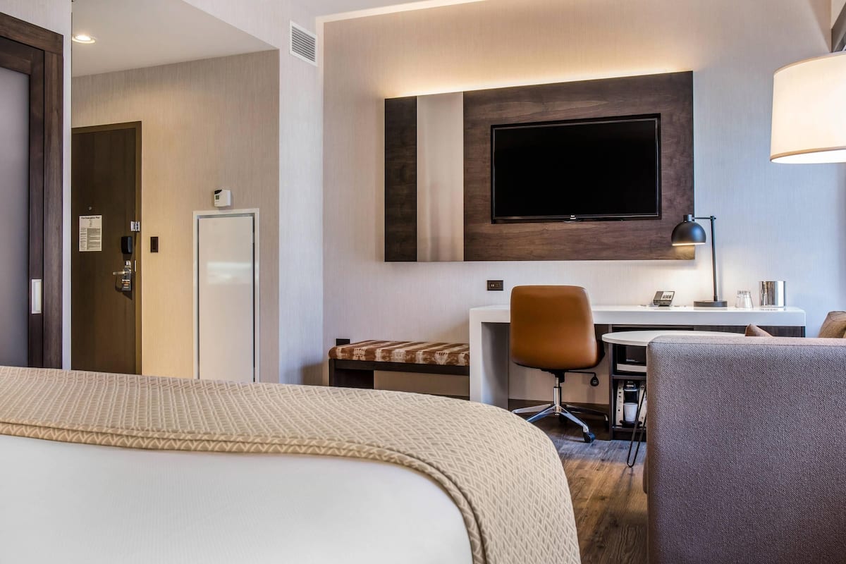 Une chambre d’hôtel équipée d’un lit, d’un bureau, d’une chaise, d’un téléviseur fixé au mur et d’une lampe.