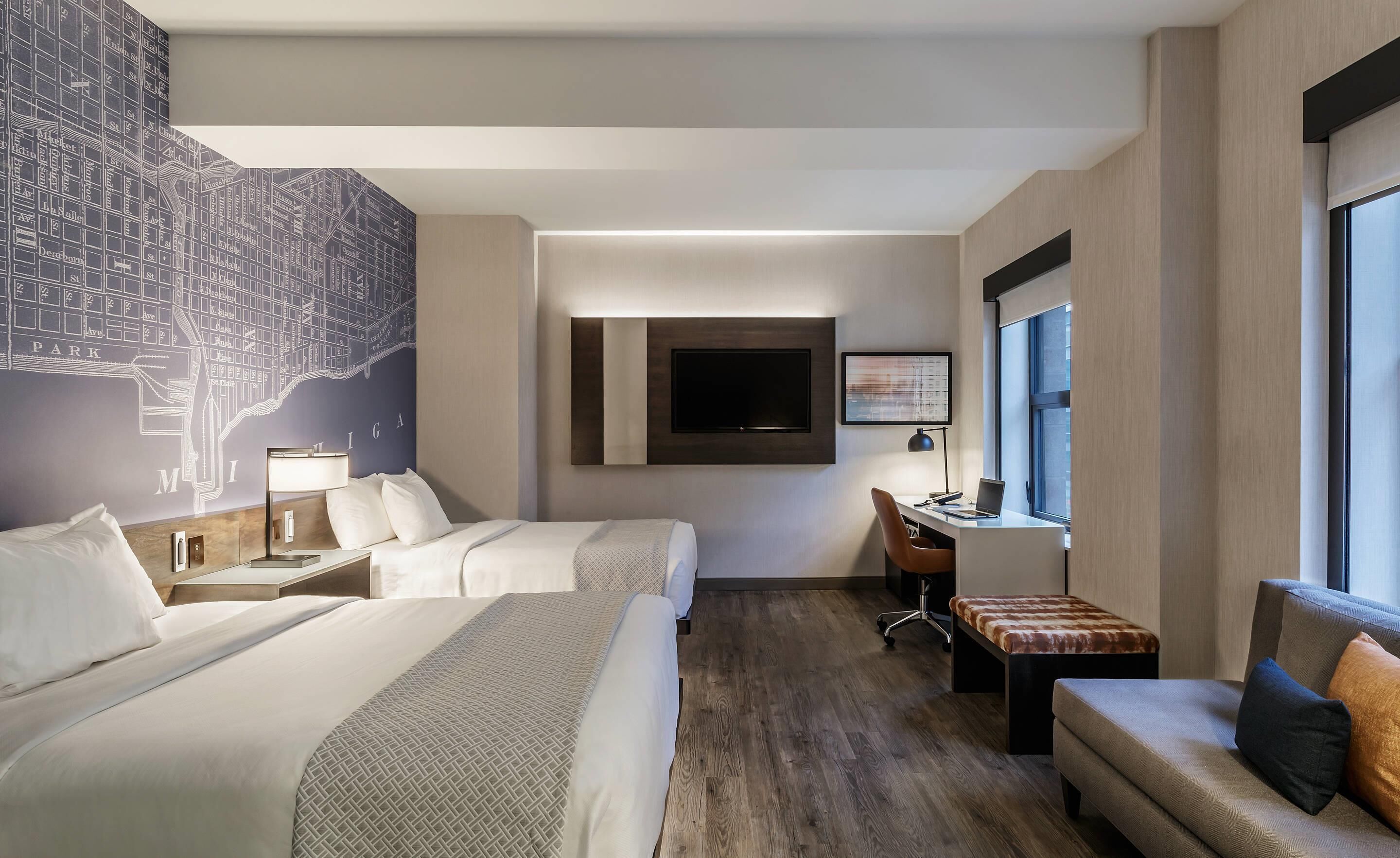 Una habitación de hotel con dos camas, un escritorio, un televisor y un ventanal grande.