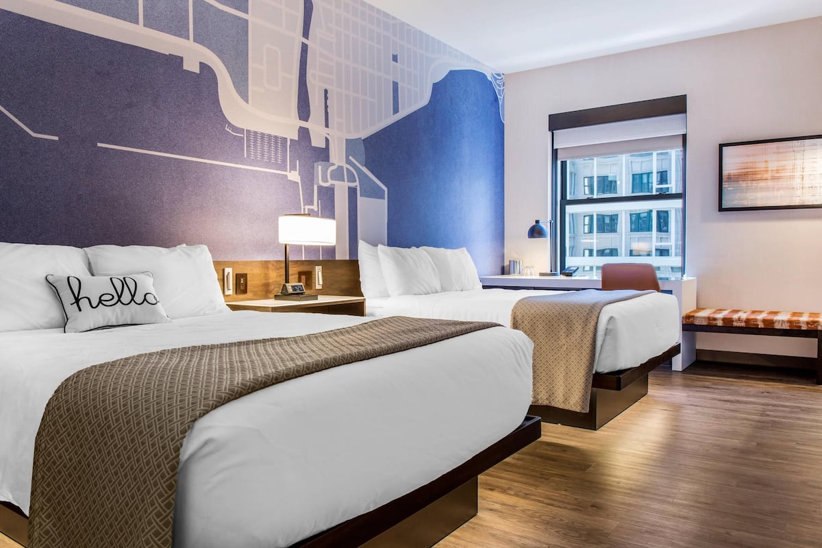 Une chambre d’hôtel avec deux lits, une grande fenêtre et une fresque représentant un paysage urbain sur le mur.