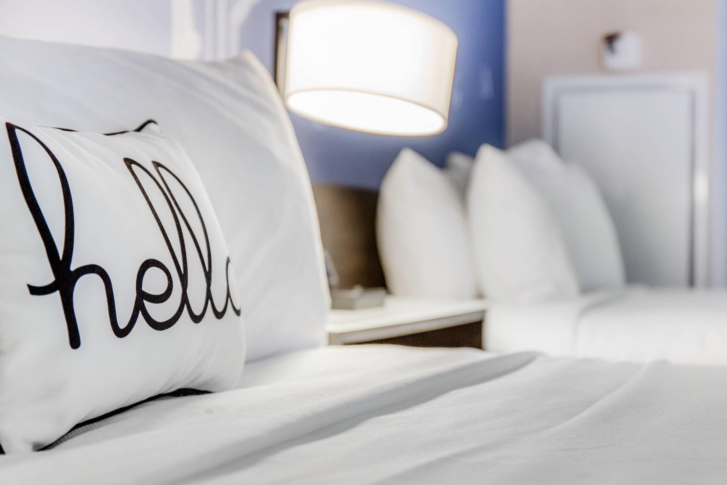 A neatly made bed with a pillow that has "hello" written on it.