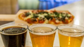 Três copos de cerveja sobre uma mesa de madeira, com uma pizza ao fundo.
