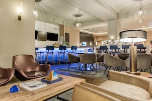 A modern hotel lobby with a bar area, seating arrangements, and a television screen.