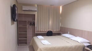 Et hotelværelse med seng, skrivebord, garderobeskab og aircondition.