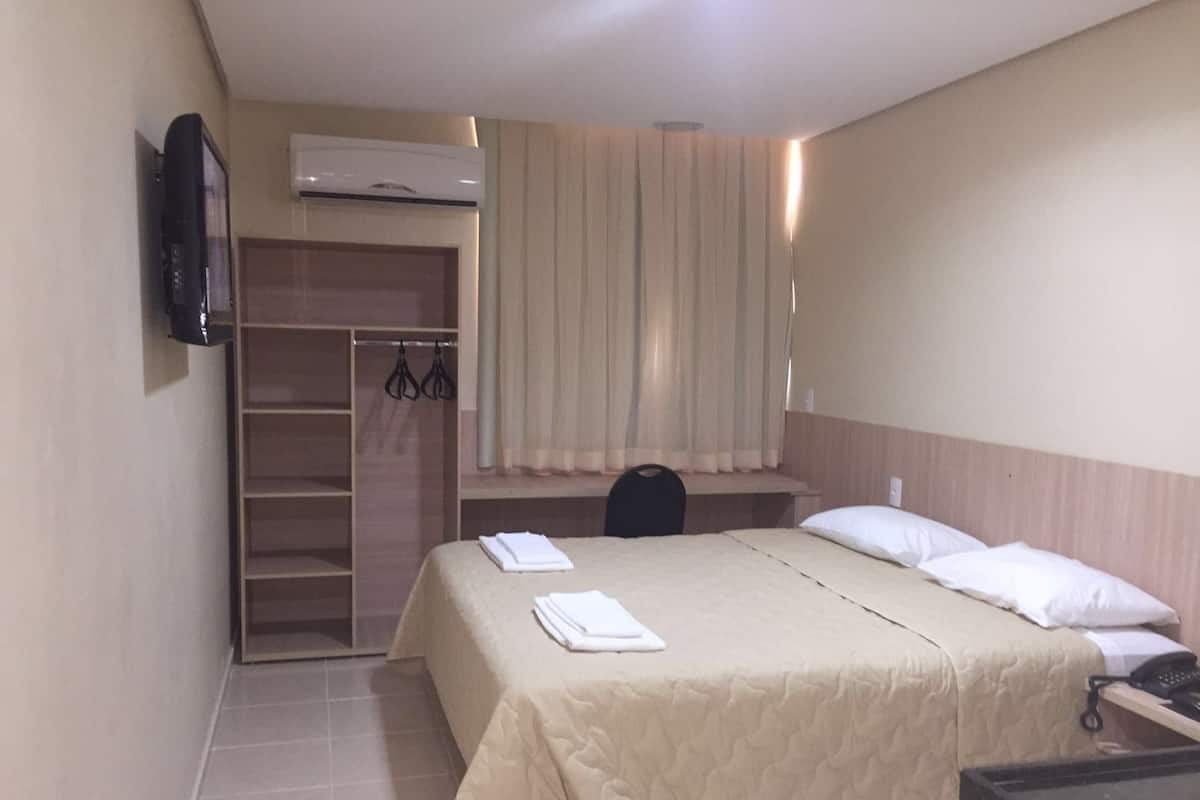 A hotel room with a bed, a desk, a wardrobe, and an air conditioning unit.