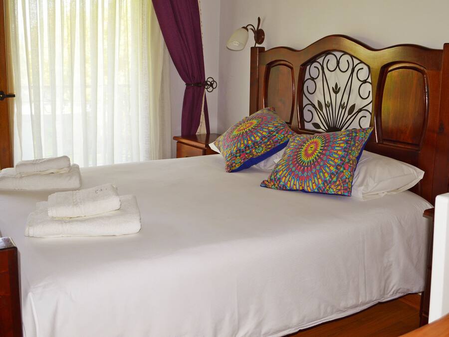 A neatly made bed with white linens and two colorful pillows, a wooden headboard, and a bedside table with a lamp.