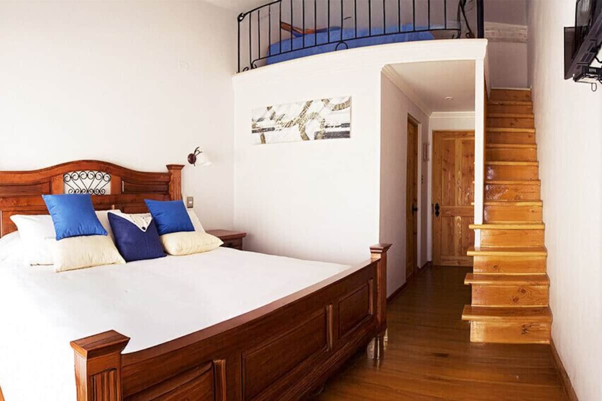 A bedroom with a large bed, wooden headboard, and a staircase leading to an upper level.