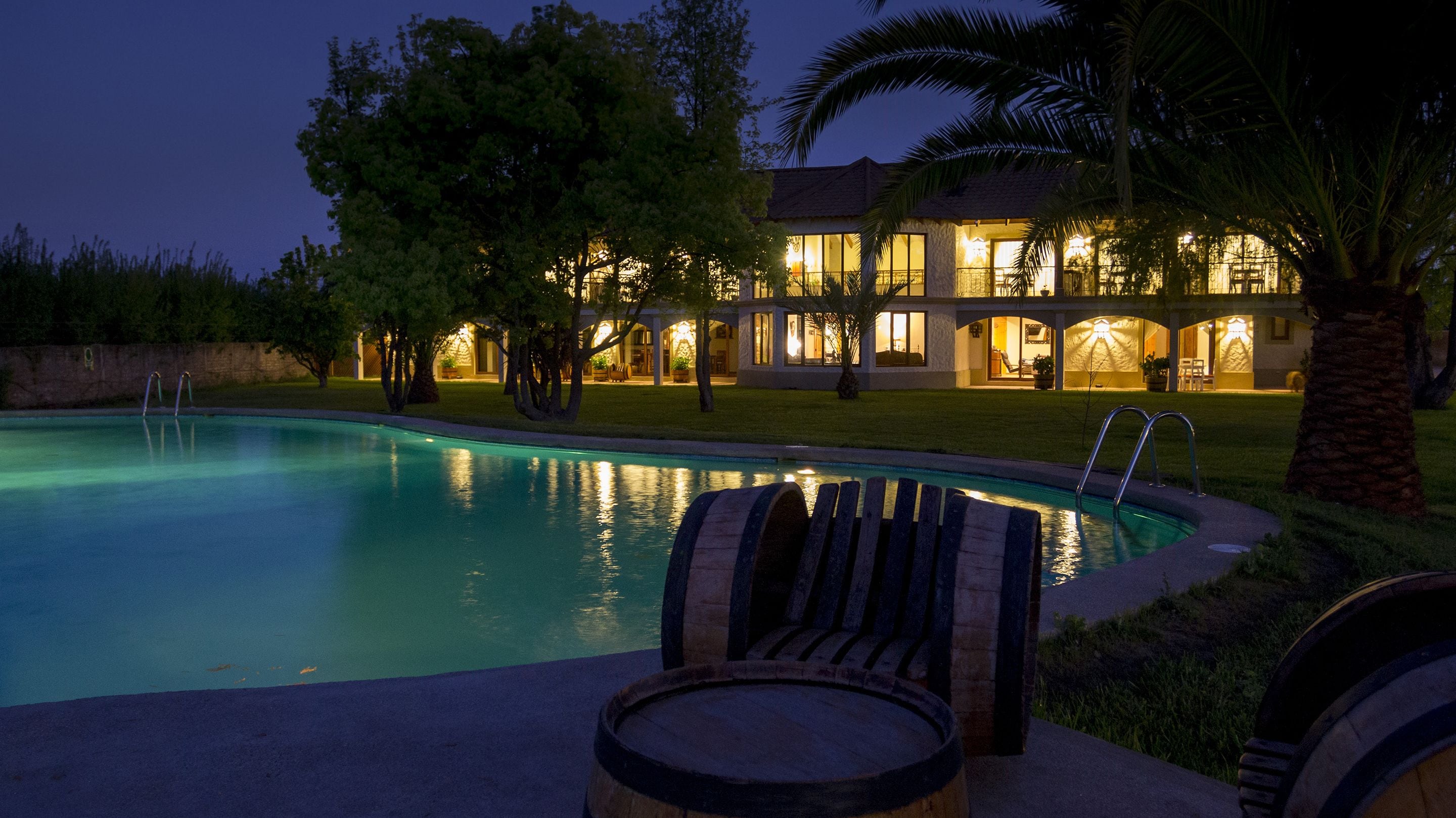 Une piscine avec des chaises longues et un bâtiment bien éclairé en arrière-plan.