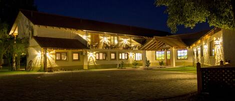 A two-story building with a tiled roof and multiple windows, illuminated by exterior lighting.