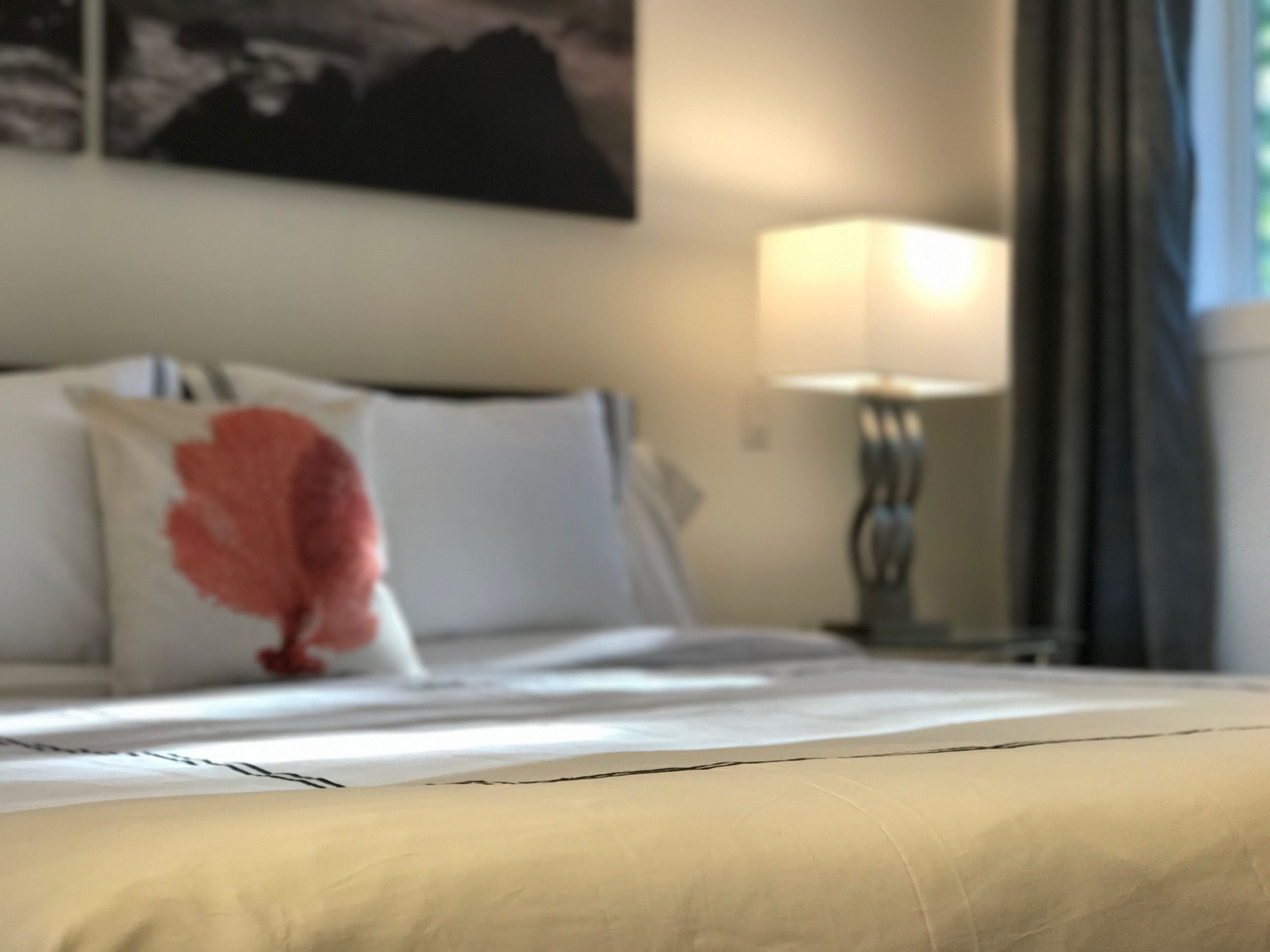 Un lit avec un oreiller blanc et rose, une lampe et un tableau accroché au mur.