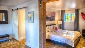 A bedroom with a wooden bed frame, a bench, a framed picture, and a window with curtains. - The Francis Boutique Inn (Ucluelet)
