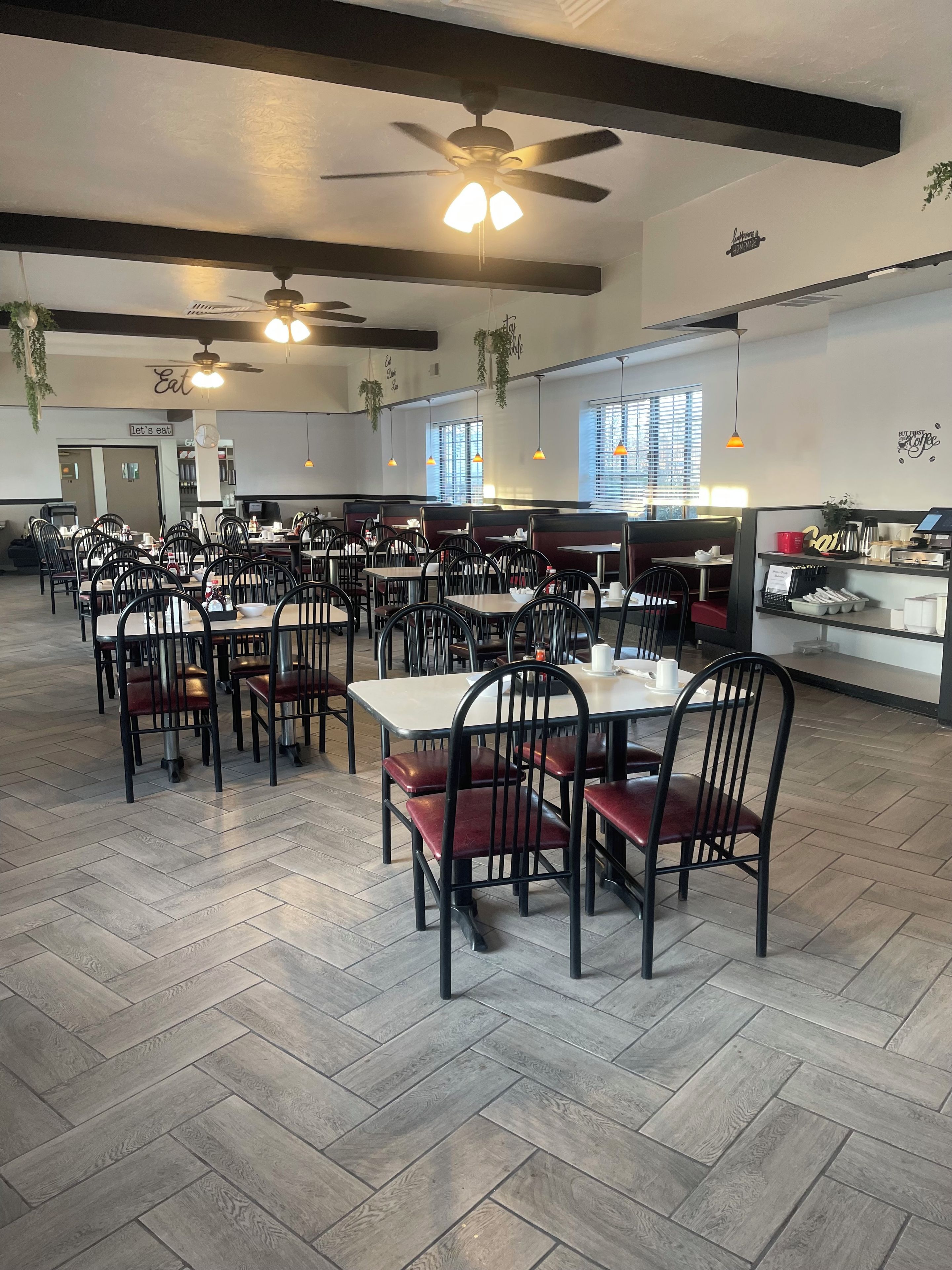 A restaurant with multiple tables and chairs, ceiling fans, and hanging plants.