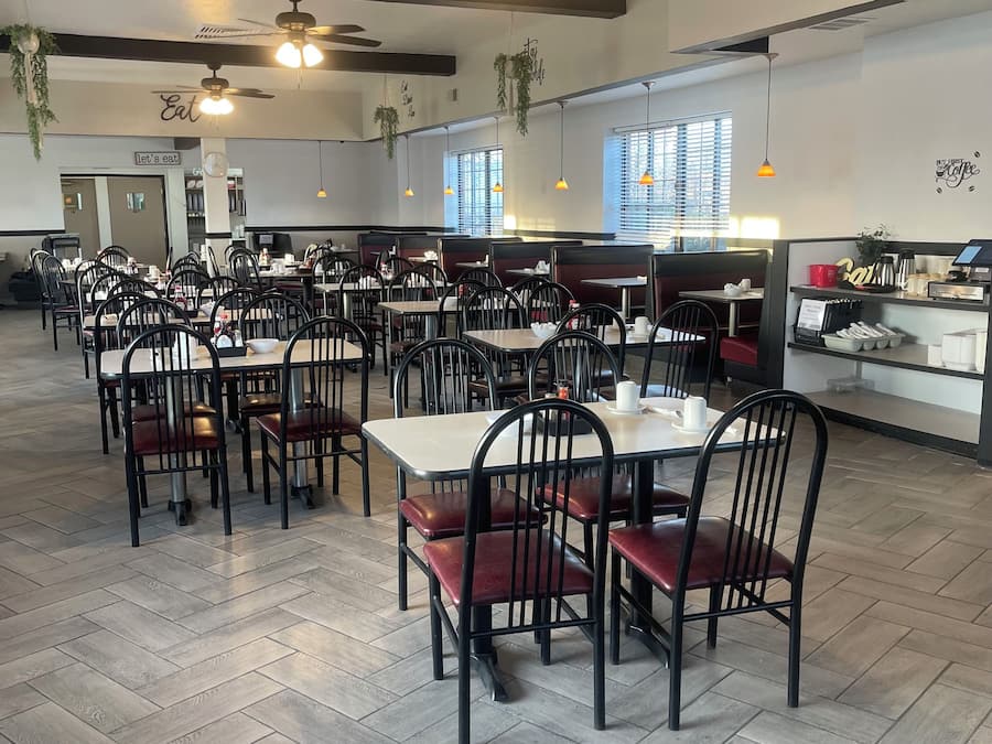 A restaurant with multiple tables and chairs, ceiling fans, and hanging plants.