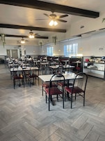 Un restaurante con varias mesas y sillas, ventiladores de techo y plantas colgantes.