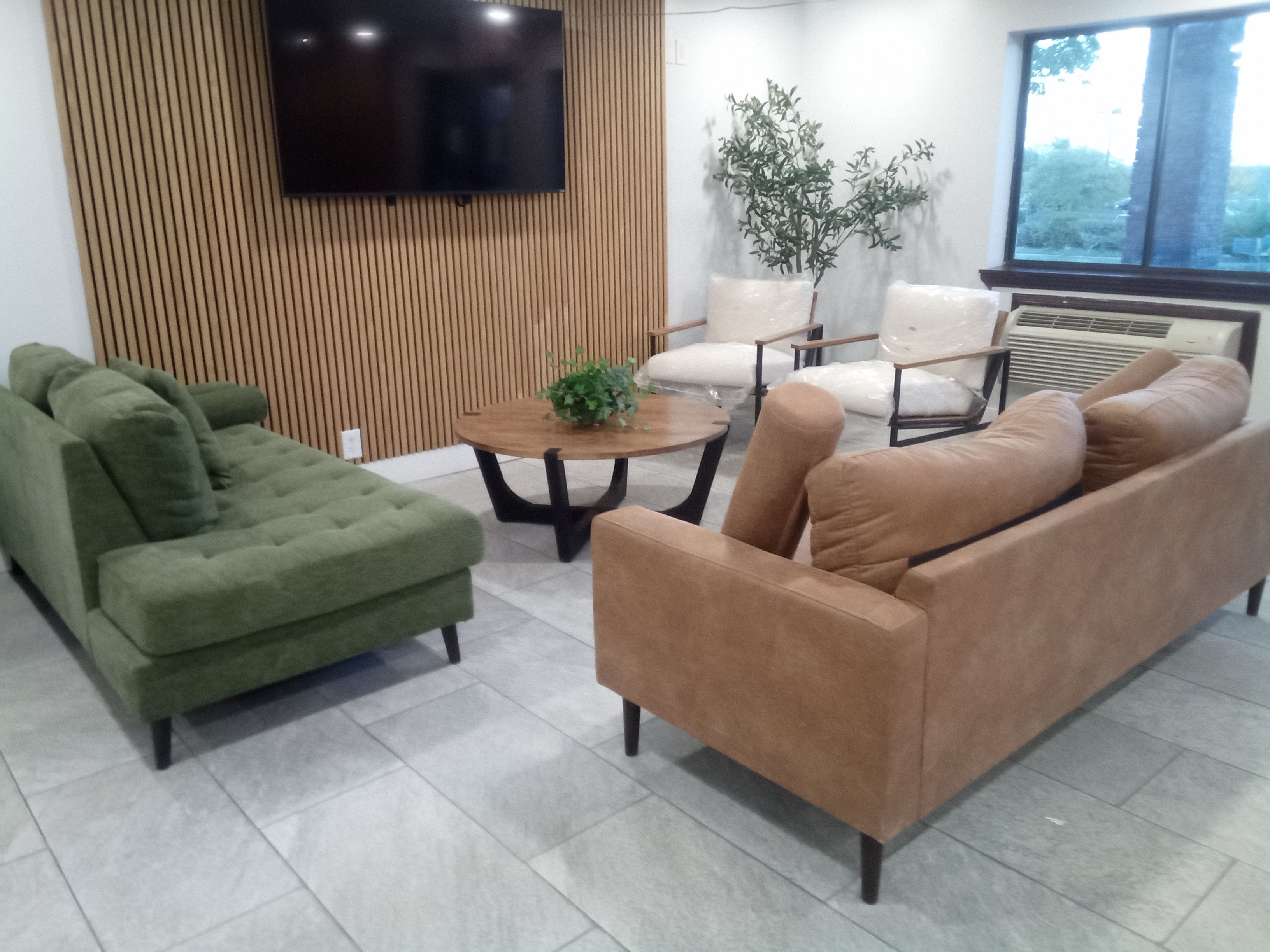 Uma sala de estar moderna com uma poltrona verde, um sofá marrom, uma mesa de centro e uma televisão fixada em uma parede de madeira.