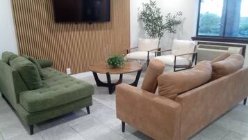 Uma sala de estar moderna com uma poltrona verde, um sofá marrom, uma mesa de centro e uma televisão fixada em uma parede de madeira.