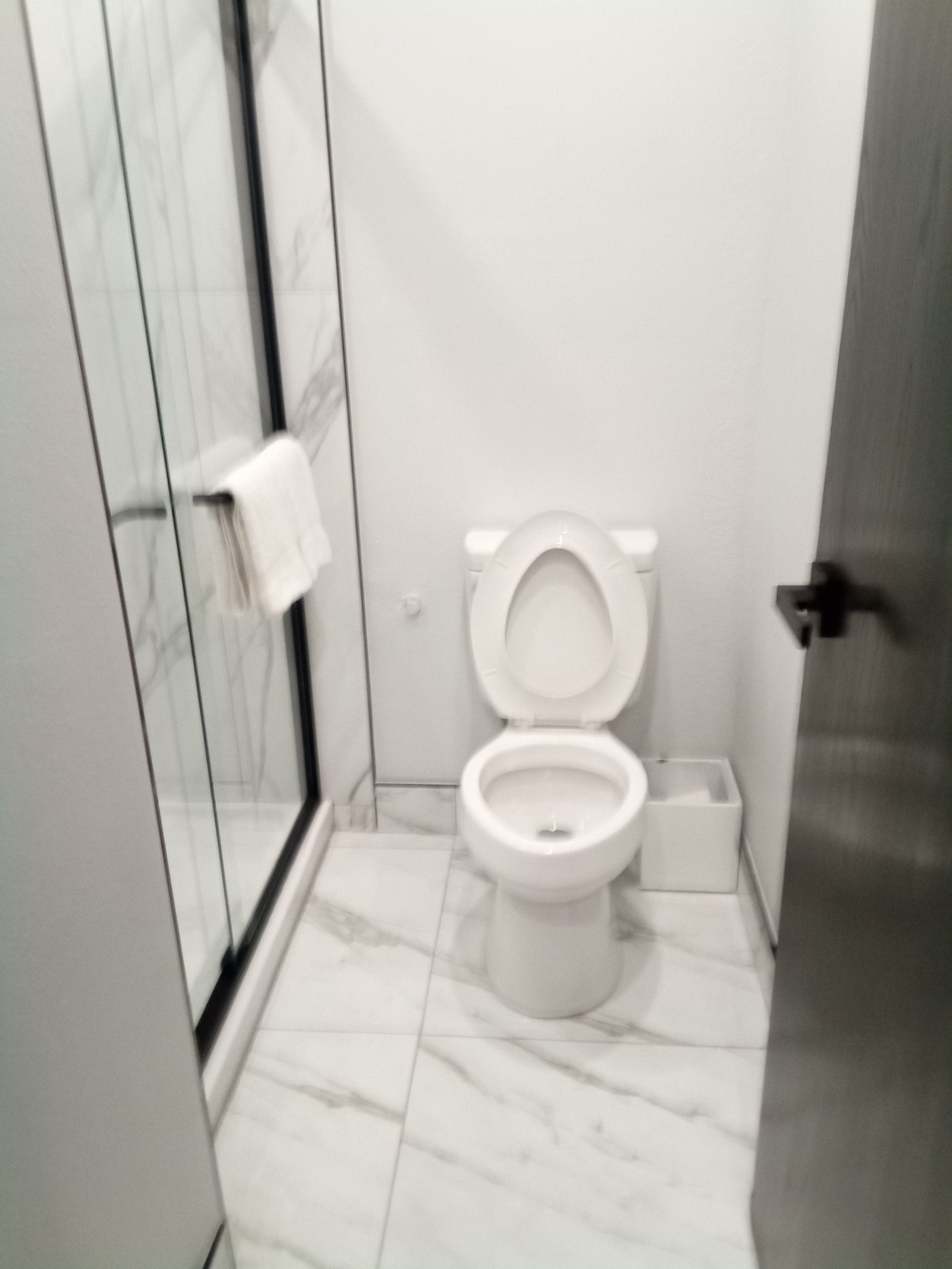 Een badkamer met toilet, een glazen douchecabine en een marmeren vloer.