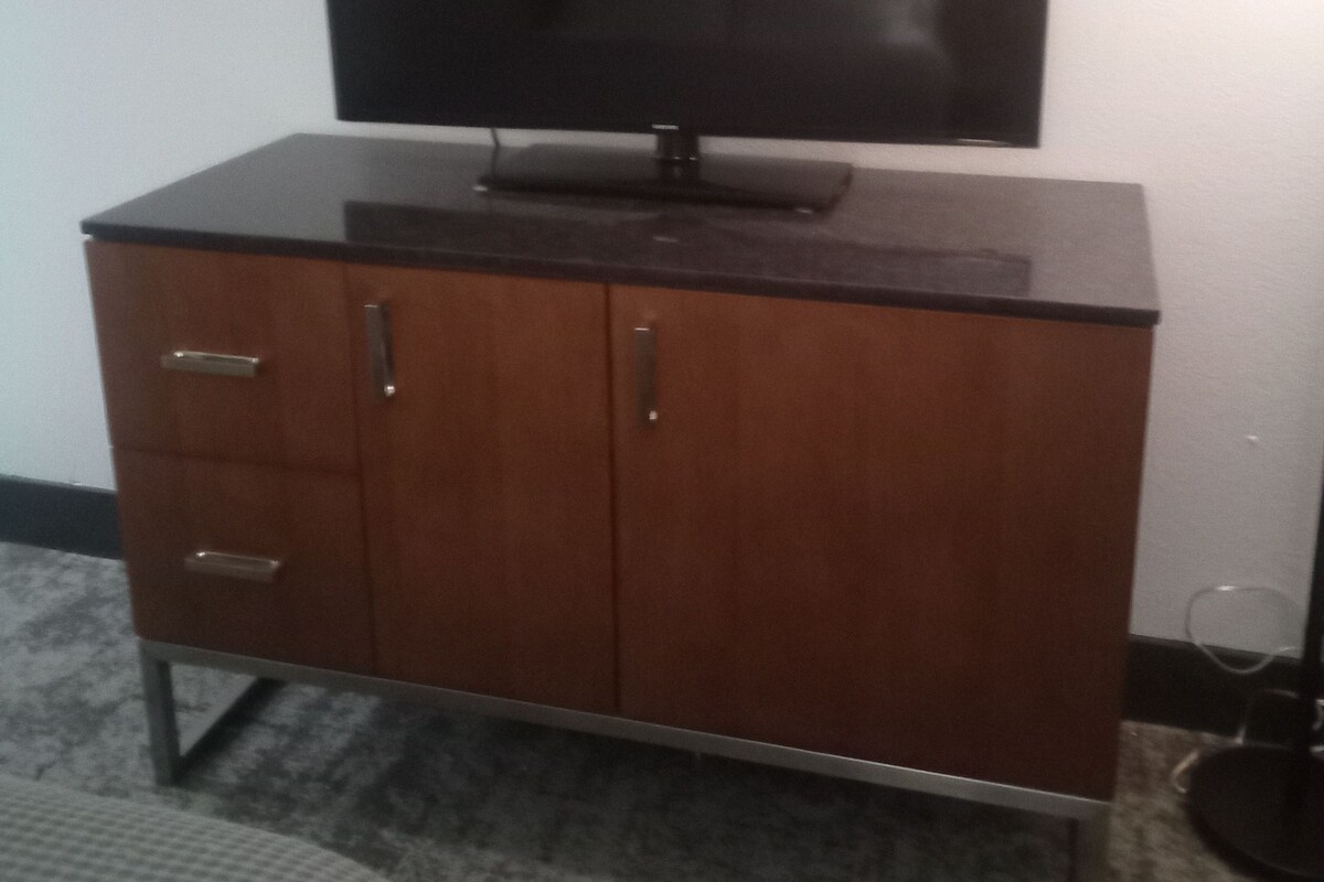 Televisor de pantalla plana montado sobre un mueble de madera con dos cajones y un pequeño estante.