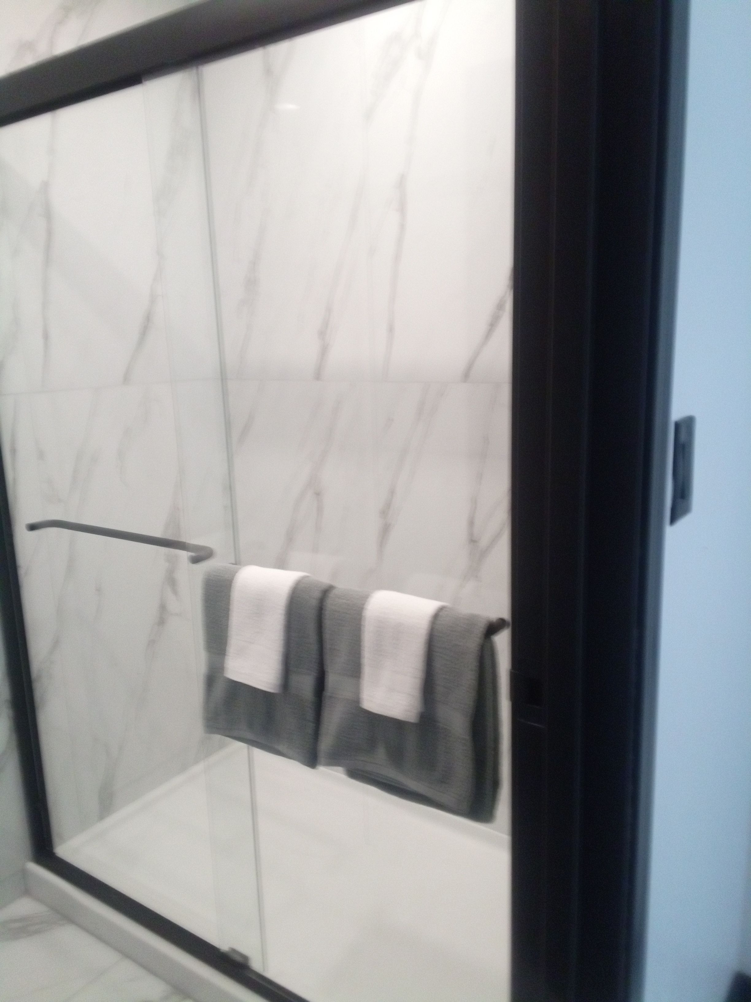 Ducha con puerta de vidrio, barra de toallas con dos toallas y pared de mármol.