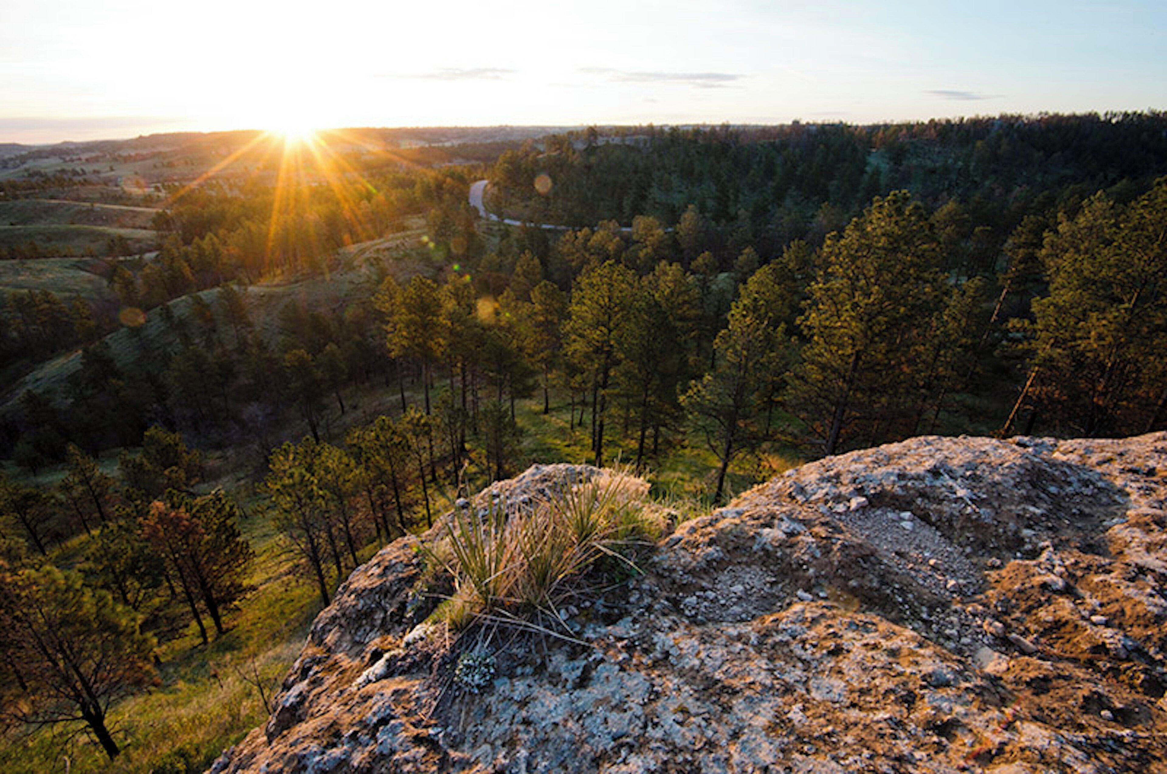 Un paysage montagneux offrant une vue dégagée sur la vallée et un coucher de soleil à l’horizon.