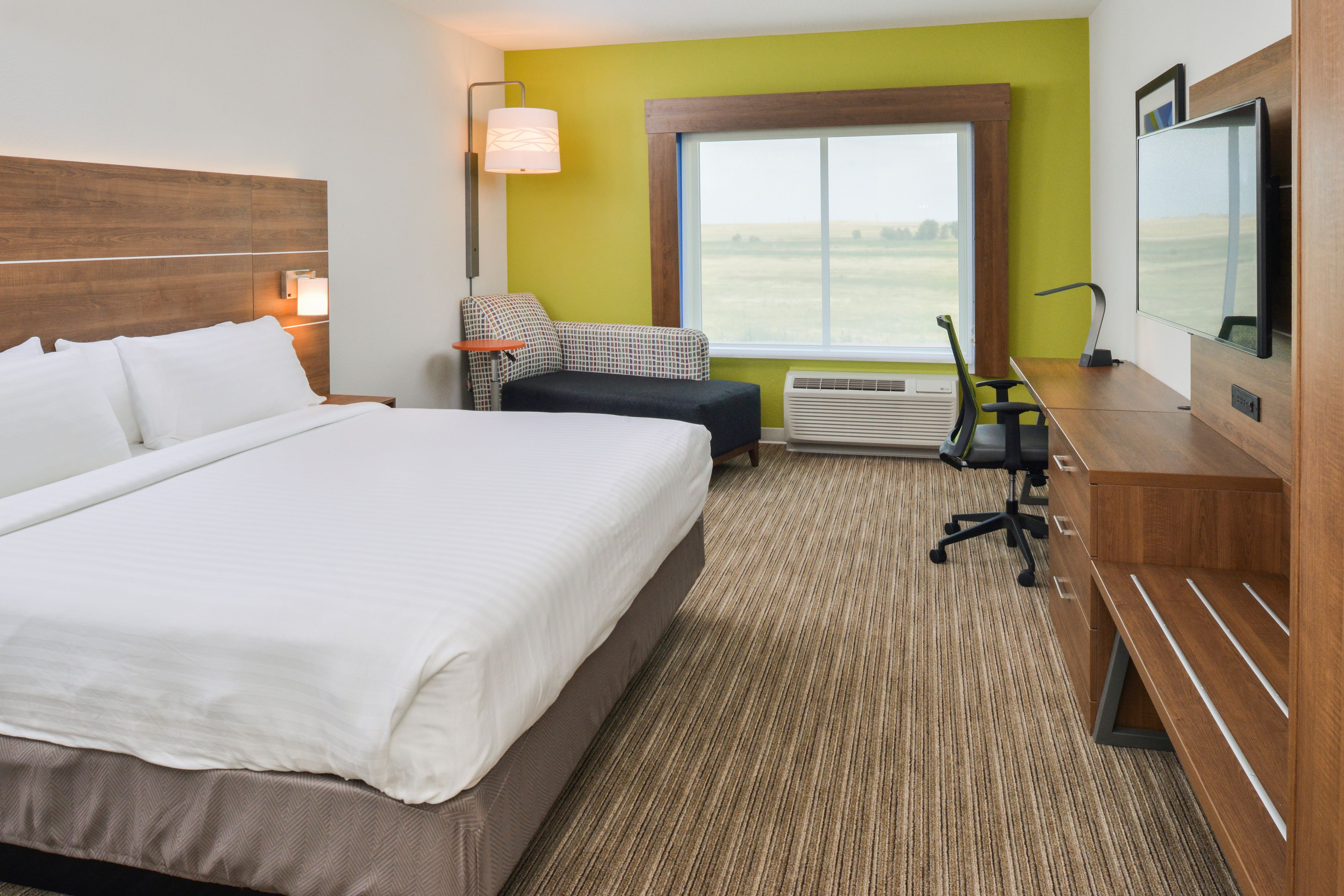A hotel room with a large bed, a desk with a chair, a sofa, a TV, and a window with a view of the outdoors.