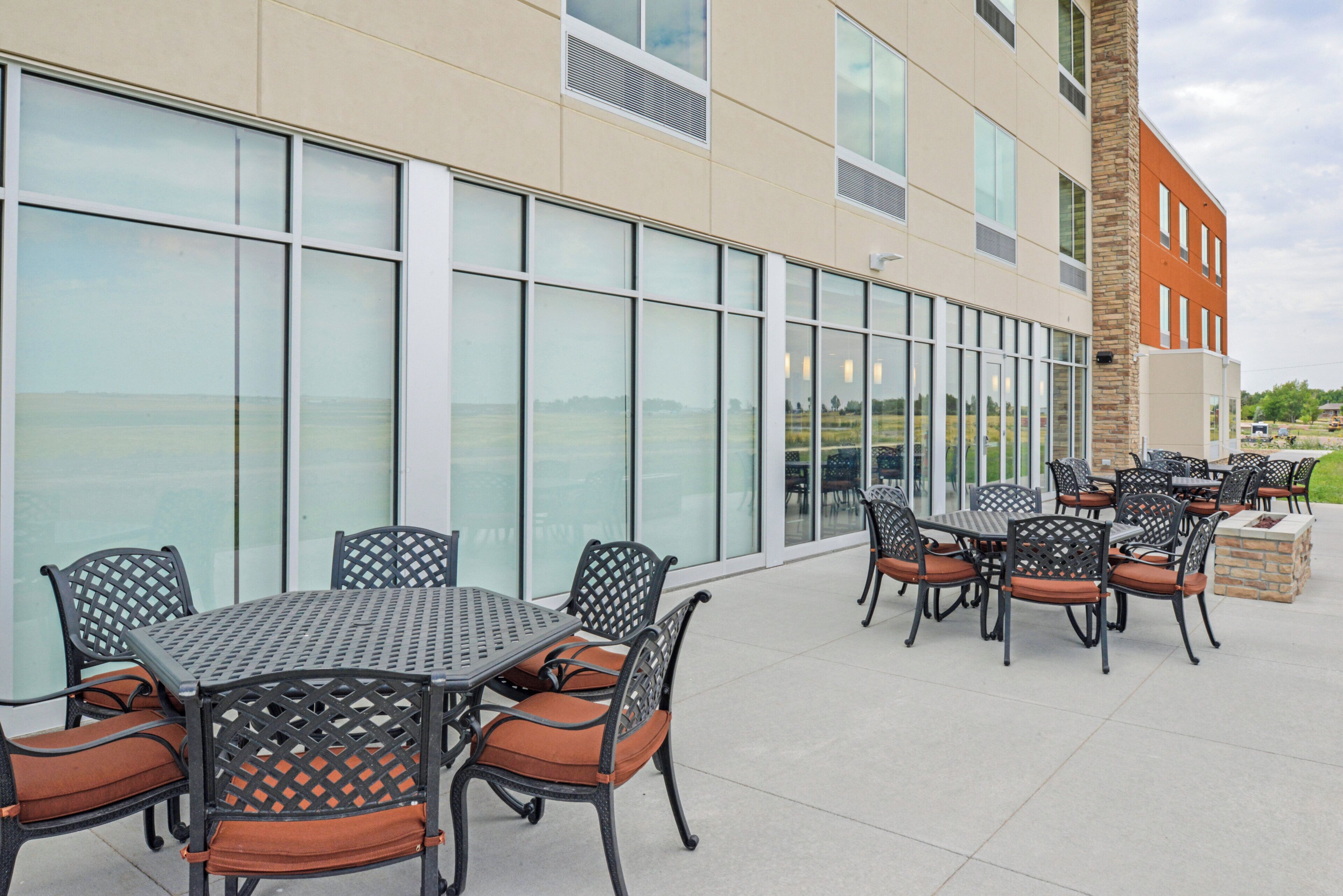 An outdoor patio with tables and chairs, a stone fireplace, and a building with large windows.