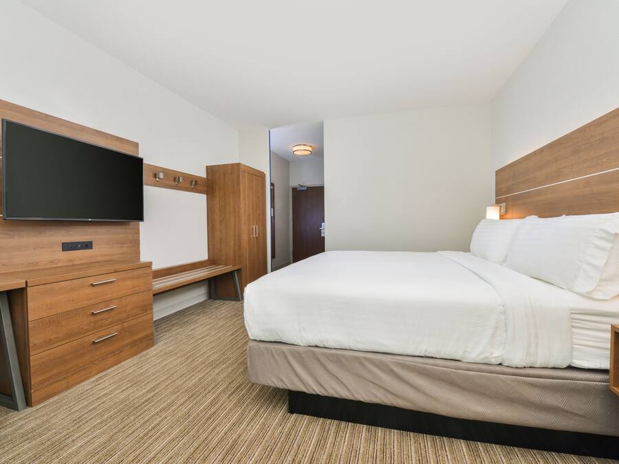 Quarto de hotel com cama, televisão presa a um móvel de madeira e escrivaninha com gavetas.