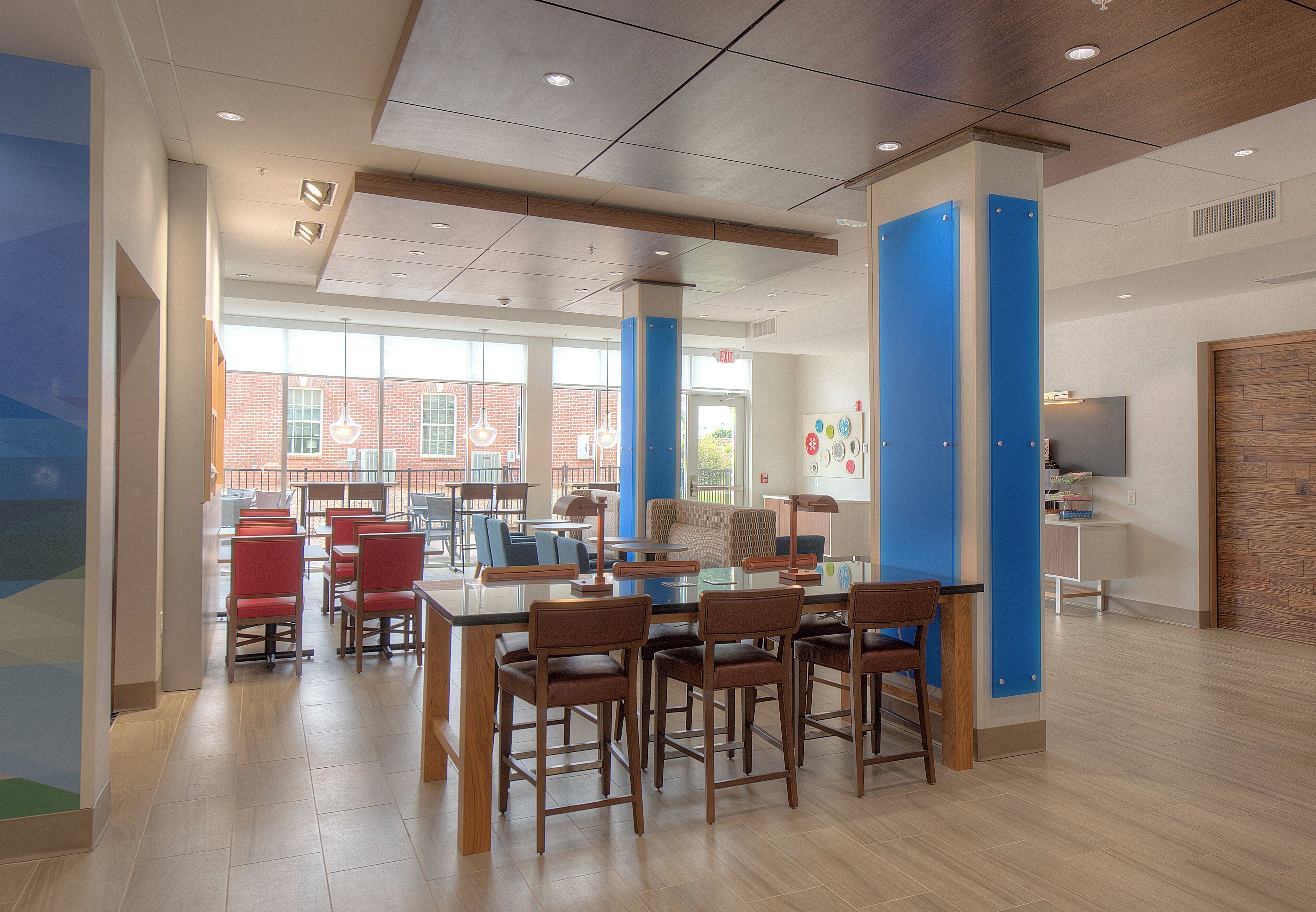 A modern interior with a dining area featuring wooden tables and chairs, a brick wall visible through large windows, and a blue accent wall.
