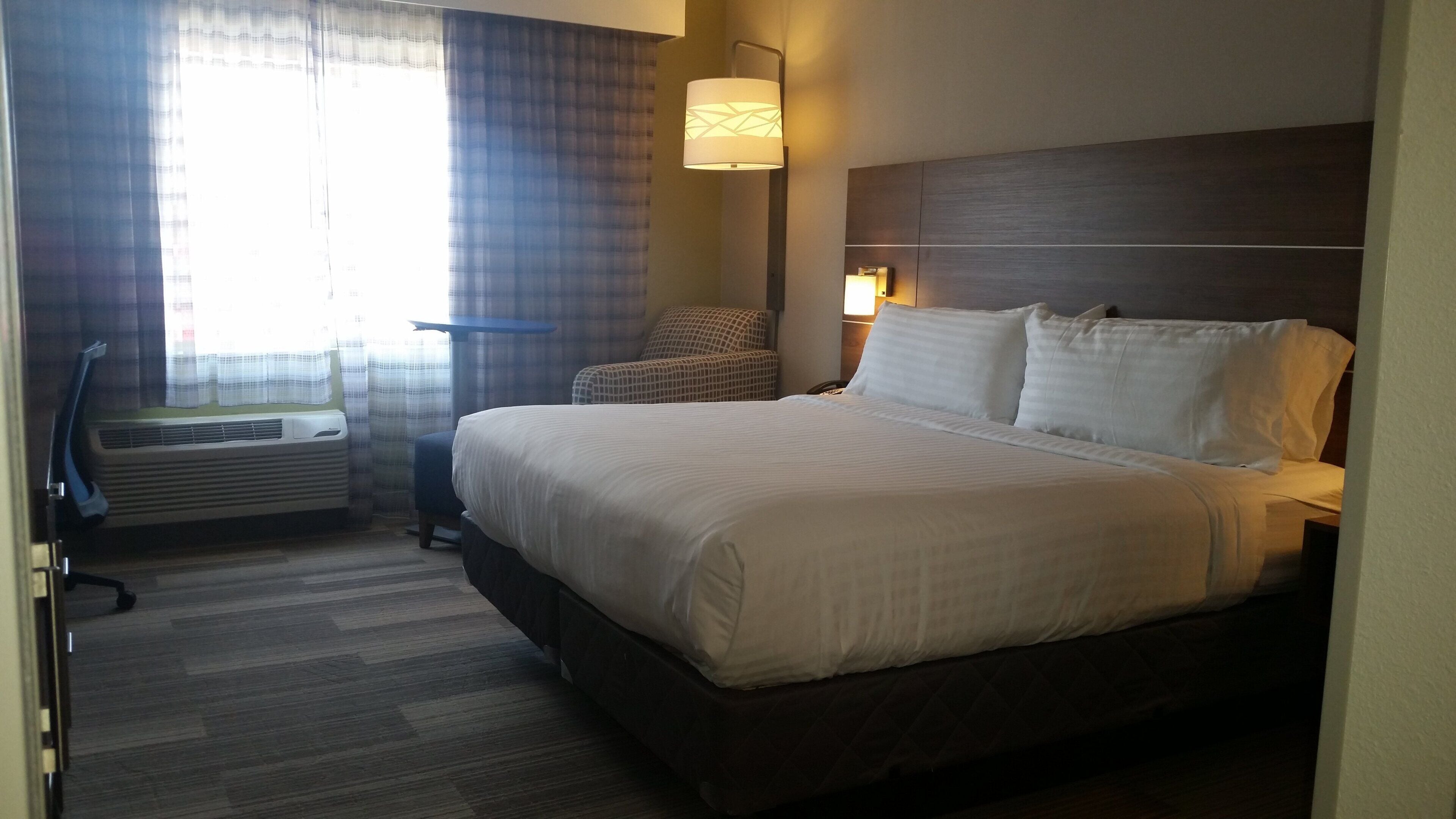 A hotel room with a large bed, a chair, a desk, and a window with curtains.