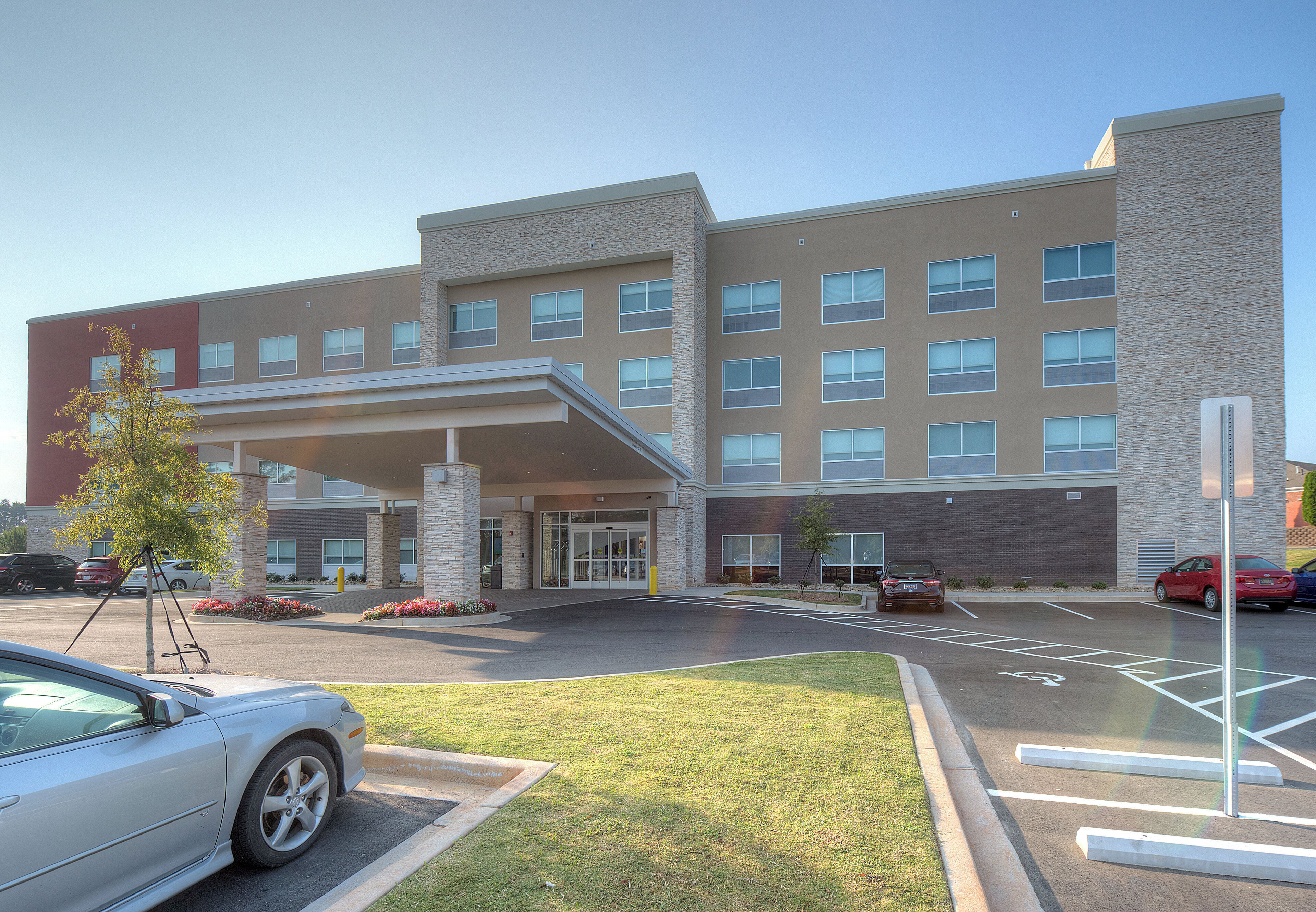 A multi-story hotel with a covered entrance, parking lot, and a landscaped area with trees.