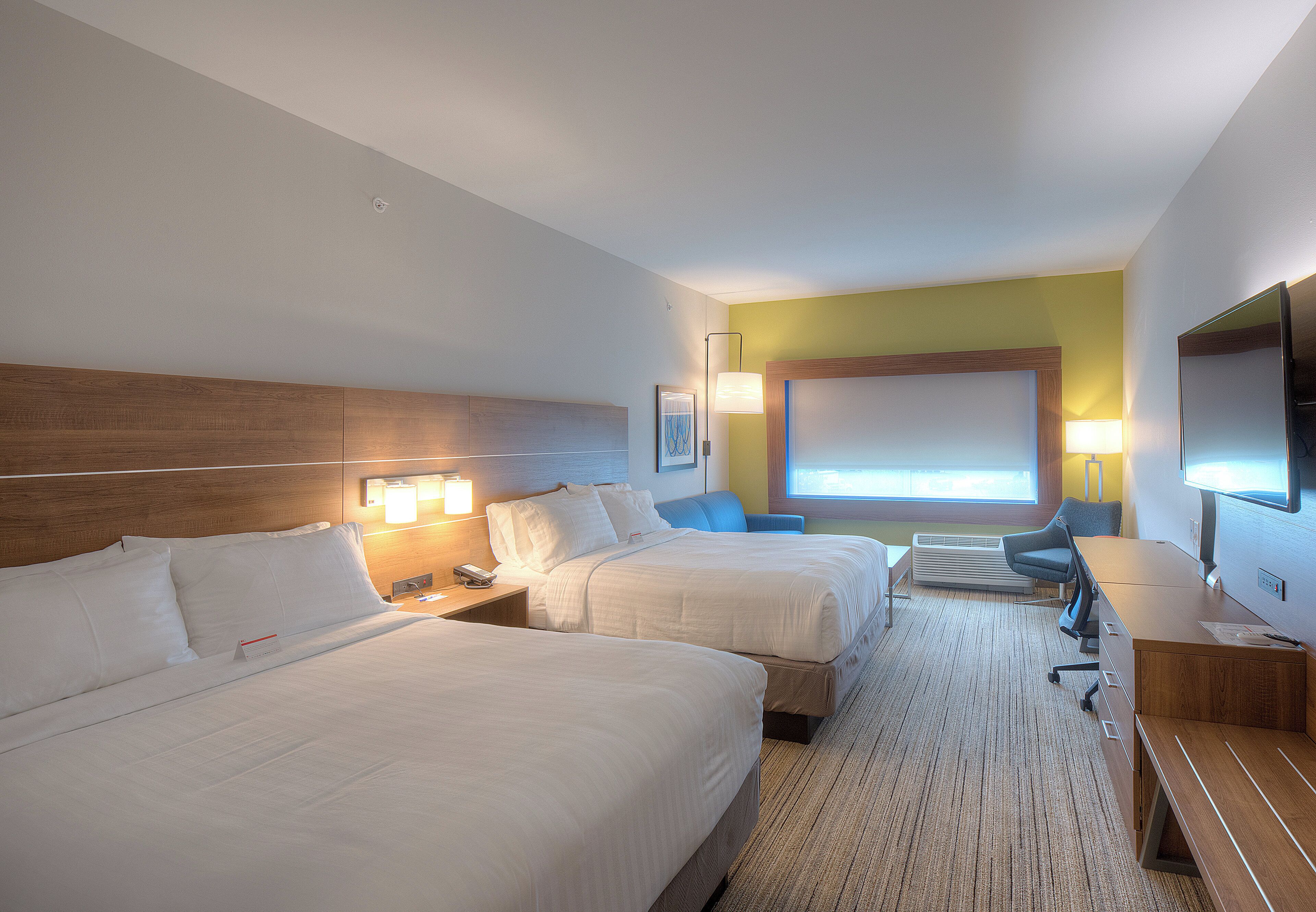 A hotel room with two beds, a desk, a chair, a TV, and a window.