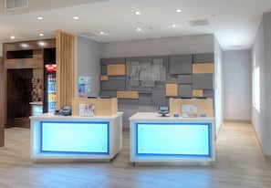 A hotel reception desk with a digital display, a Coca-Cola refrigerator, and a wall with a geometric design. - Holiday Inn Express & Suites Fort Mill by IHG (Fort Mill)