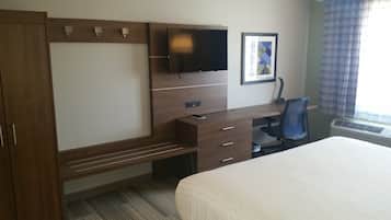 A hotel room with a bed, a desk with a chair, a flat-screen TV mounted on the wall, and a framed picture.