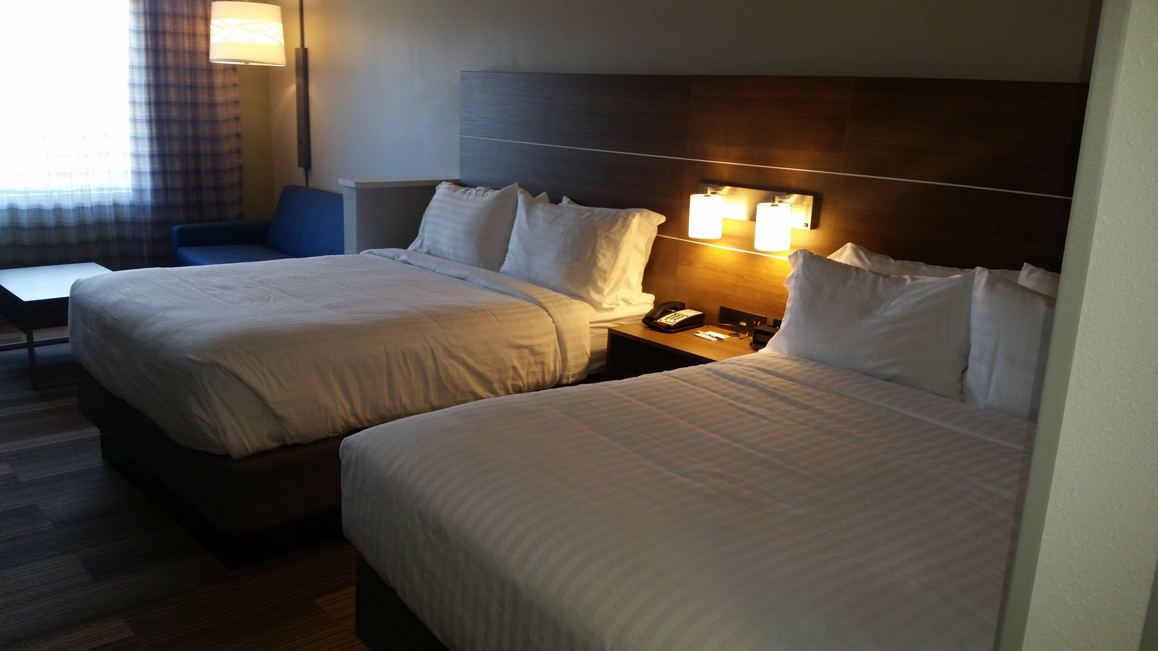 A hotel room with two beds, a desk, a chair, and a nightstand with a phone.