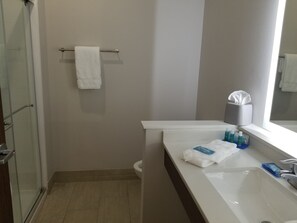 Un baño con un lavamanos blanco, un espejo, un perchero para toallas y artículos de aseo en el mostrador.