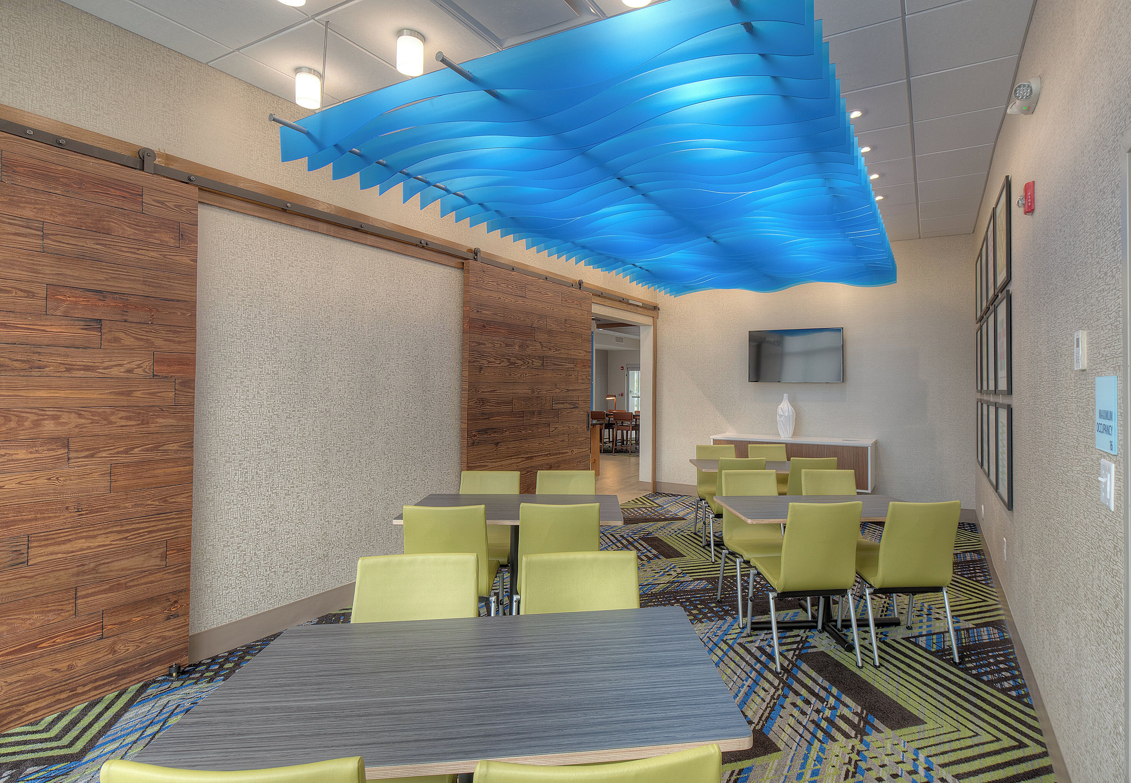 A conference room with a wooden wall, a blue ceiling feature, and green chairs.