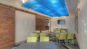 A conference room with a wooden wall, a blue ceiling feature, and green chairs.