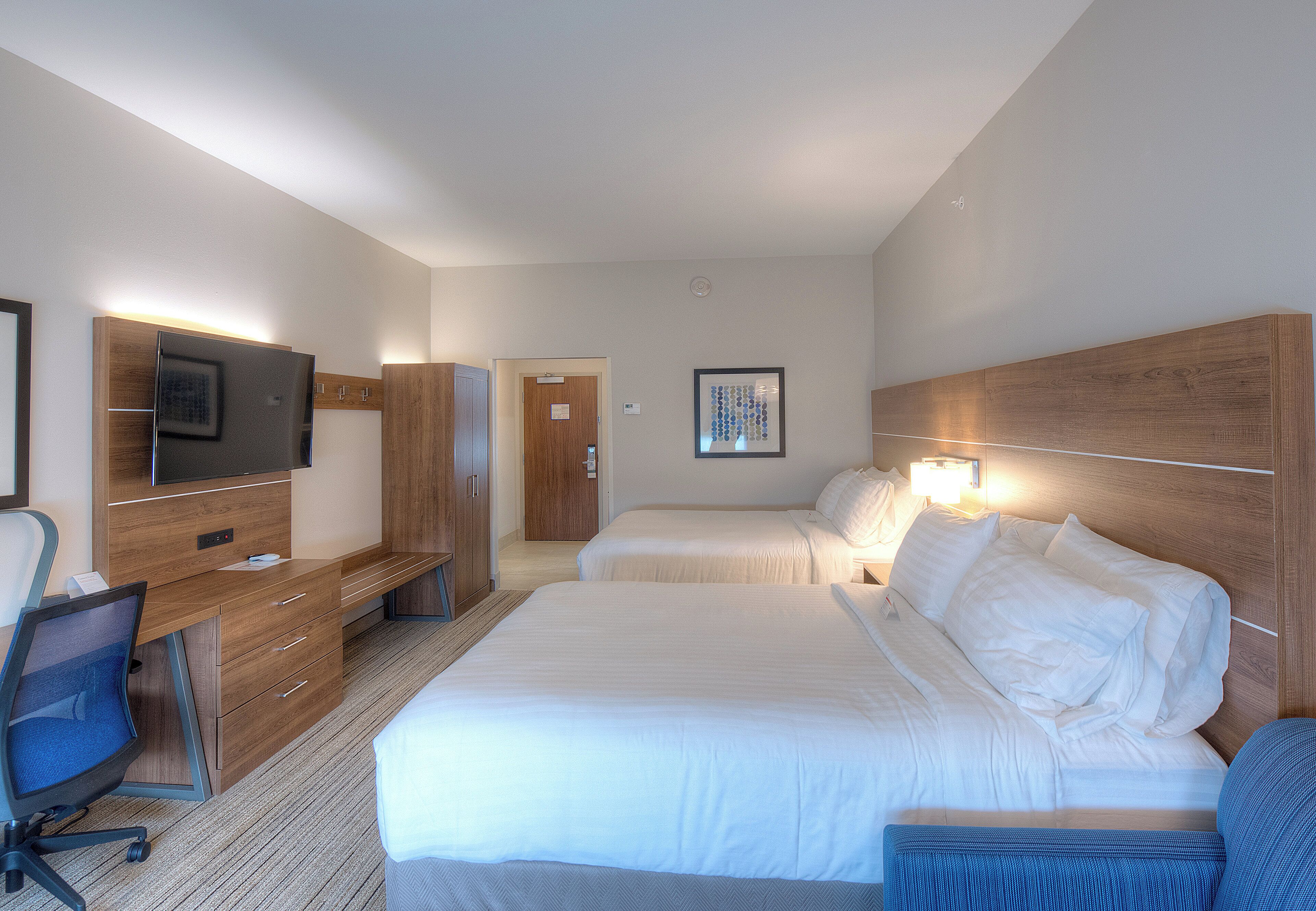 Ein Hotelzimmer mit Bett, Schreibtisch mit Stuhl, Fernseher und einer Tür.