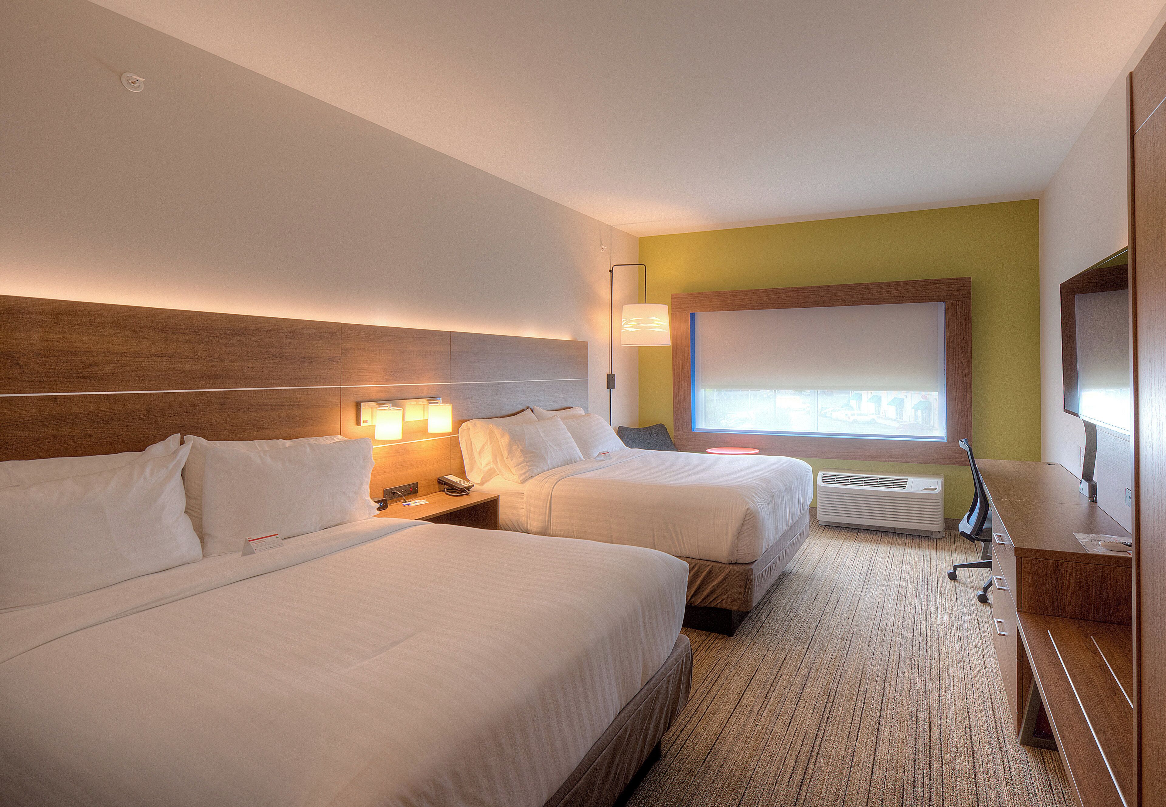 Une chambre d’hôtel avec deux lits, un bureau, une lampe et une grande fenêtre.
