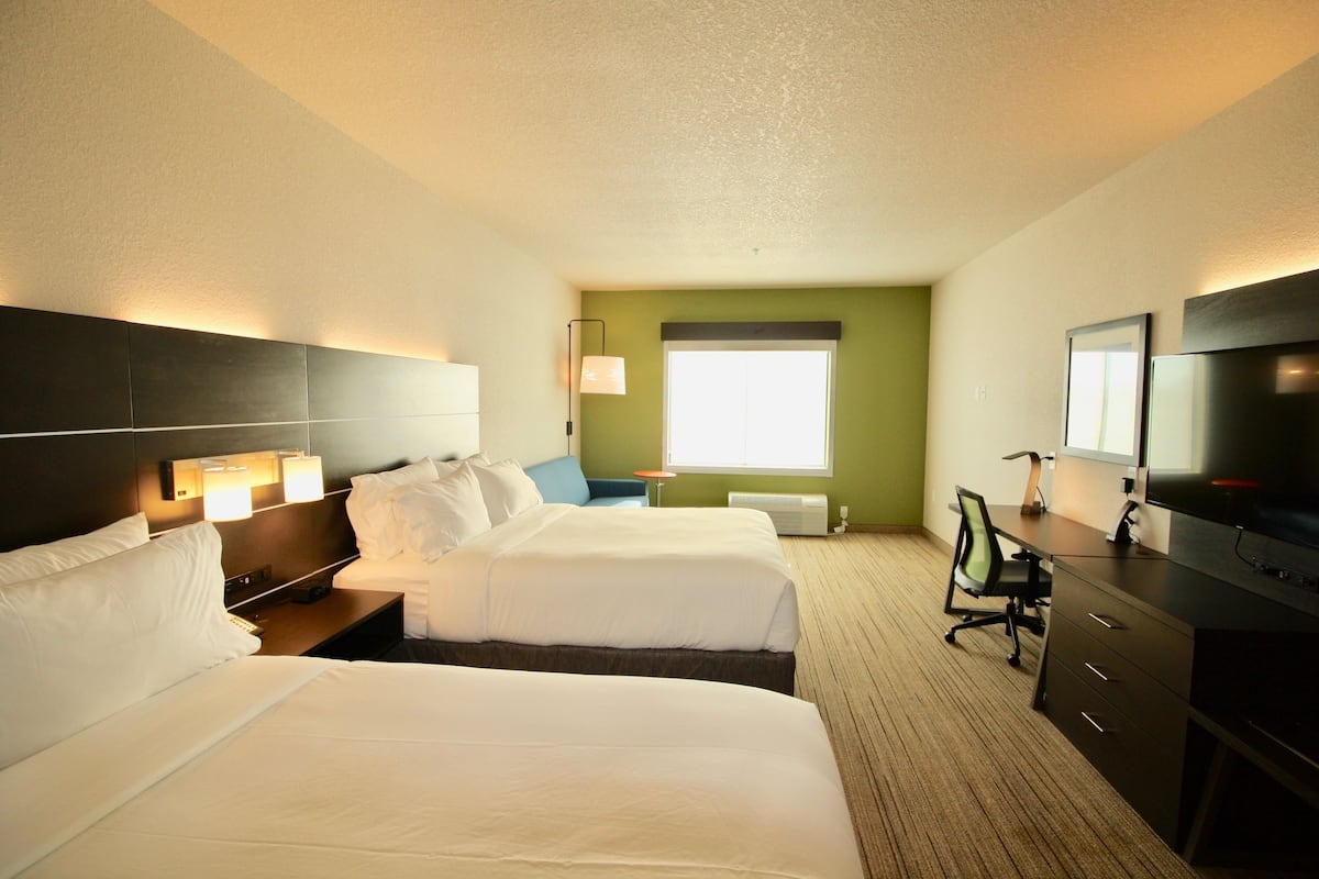 A hotel room with two beds, a desk, a chair, a TV, and a window with blinds.
