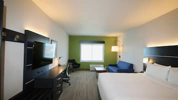 A hotel room with a bed, a desk with a flat-screen TV, a chair, a small table, and a window.