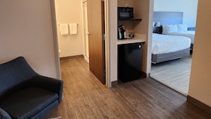 A hotel room with a wooden floor, a bed, a small kitchenette with a microwave, and a seating area with a chair. - Holiday Inn Express & Suites Camas - Vancouver by IHG (Camas)