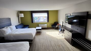 Habitación de hotel con dos camas, un televisor de pantalla plana, un escritorio y una ventana con vistas a un jardín.
