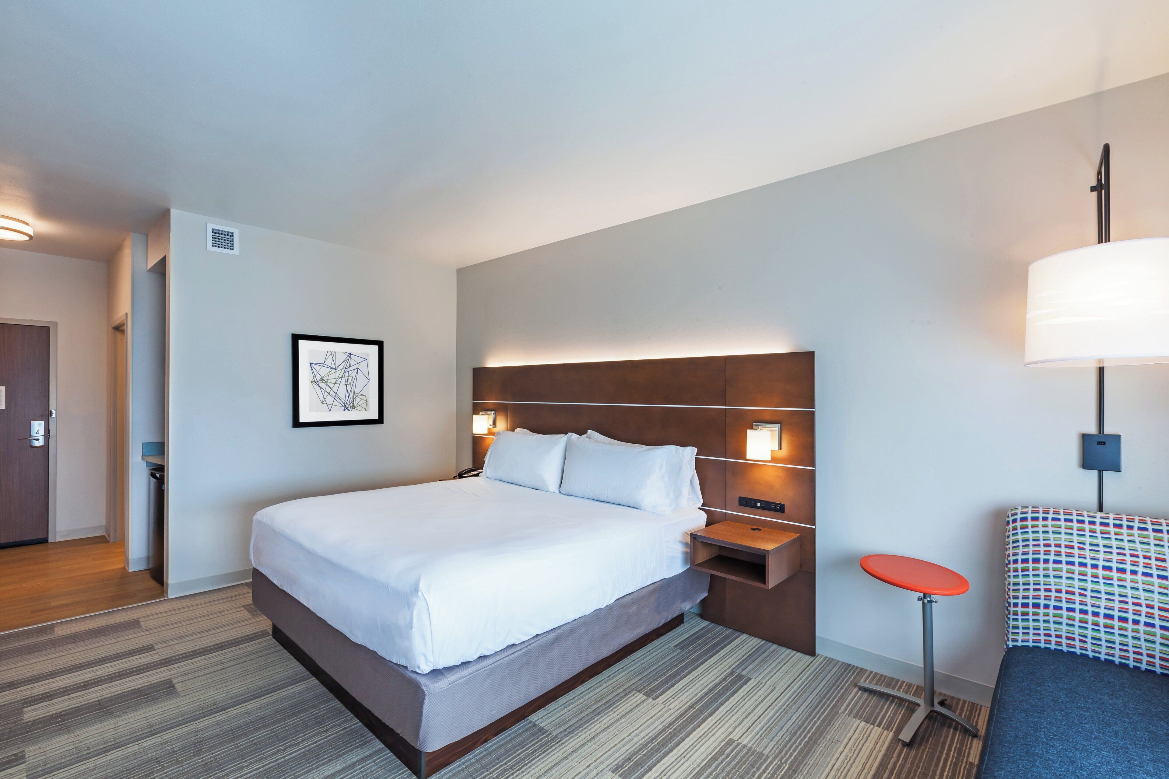 Ein Hotelzimmer mit einem großen Bett, Nachttischen, einem Schreibtisch, einem Sessel und einer Wandlampe.