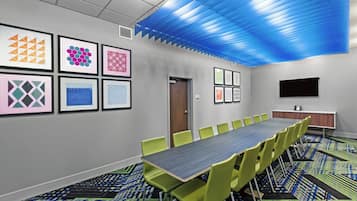 A conference room with a long table, green chairs, and framed artwork on the walls.
