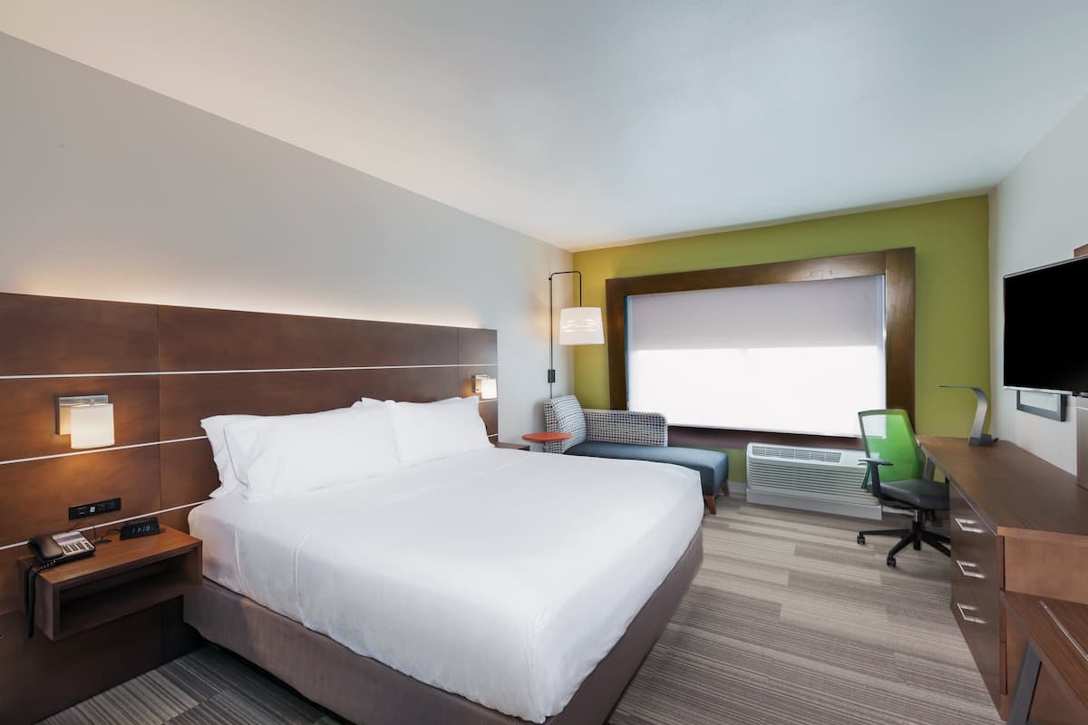 A hotel room with a large bed, a desk, a chair, a TV, and a window with a view.