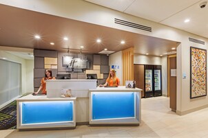 A reception area with two receptionists, a counter, a refrigerator, and a patterned wall.