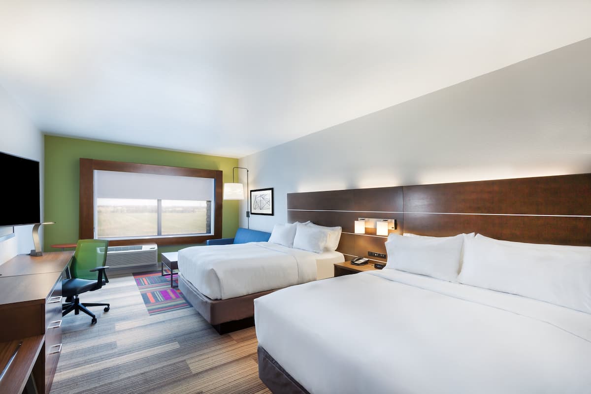 A hotel room with two beds, a desk, a chair, a TV, and a large window.