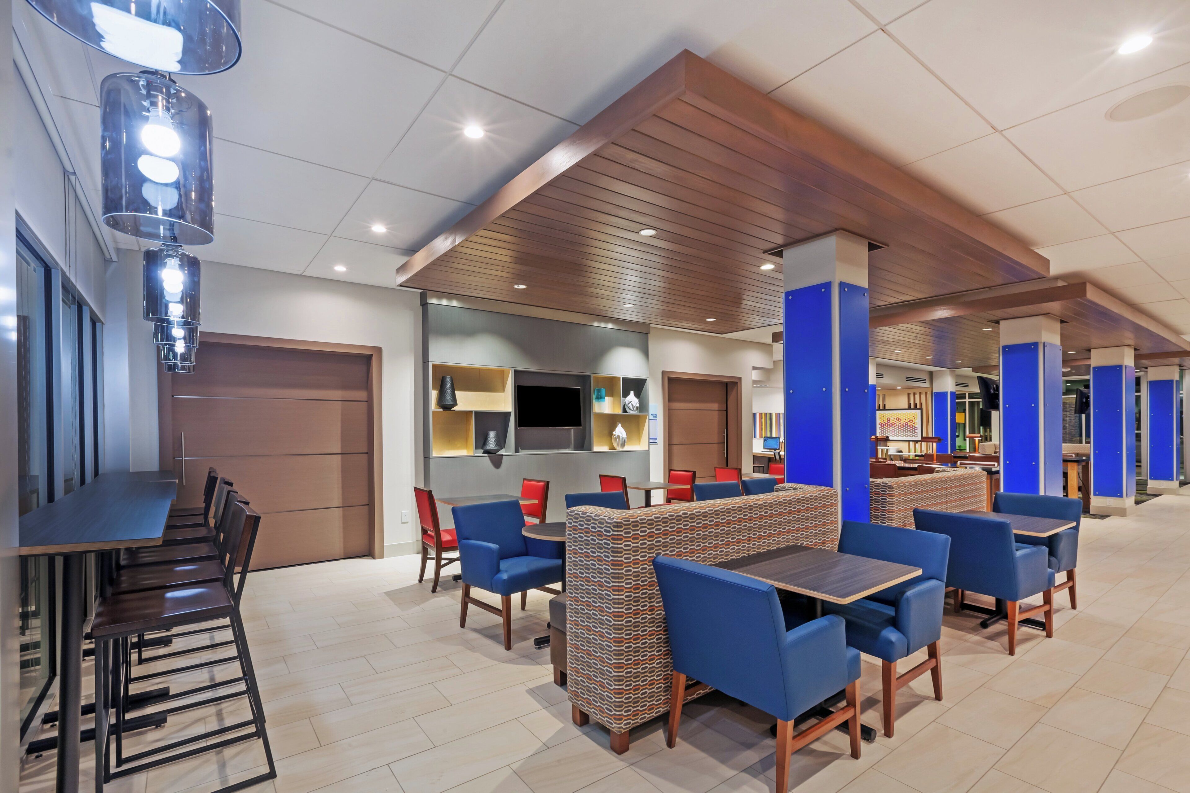 A modern restaurant with high tables and chairs, a bar area, and a seating section with patterned cushions.