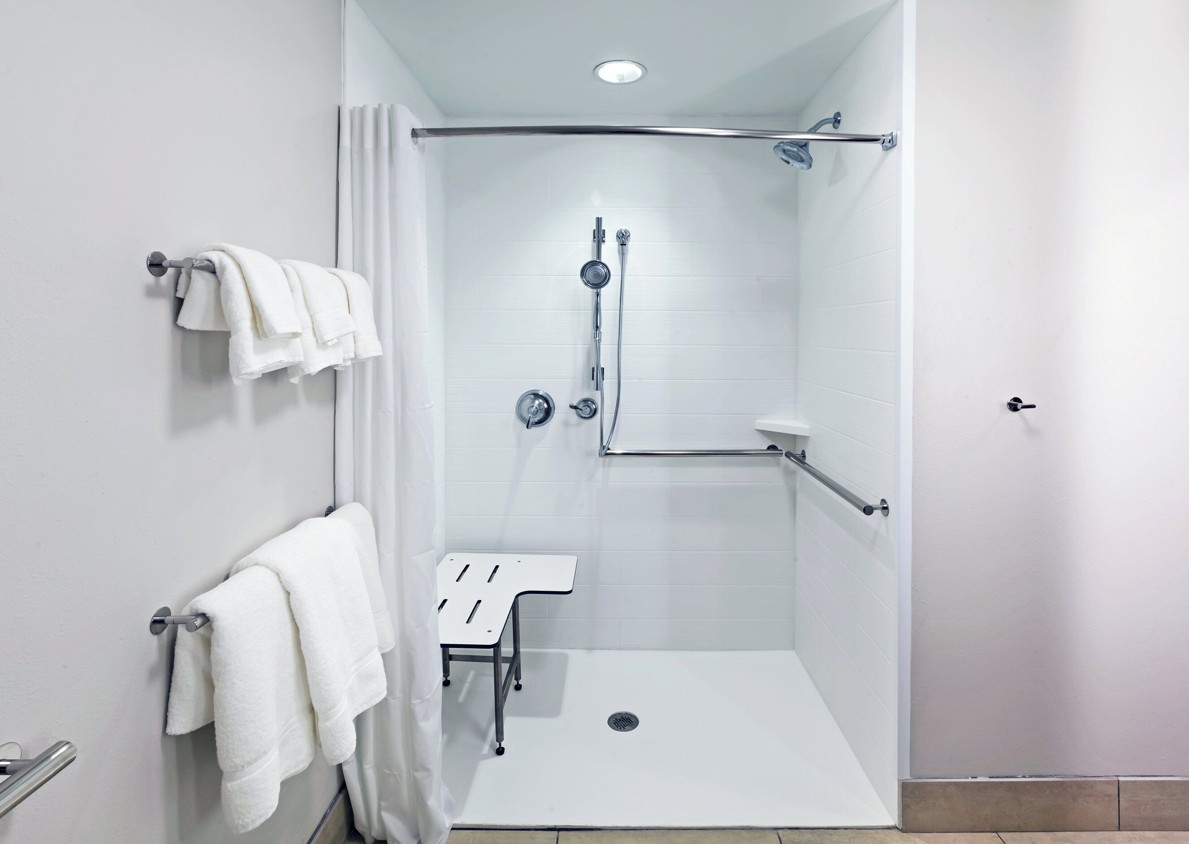 A modern shower area with a glass door, a handheld showerhead, a handheld shower head, a towel rack, and a small step stool.
