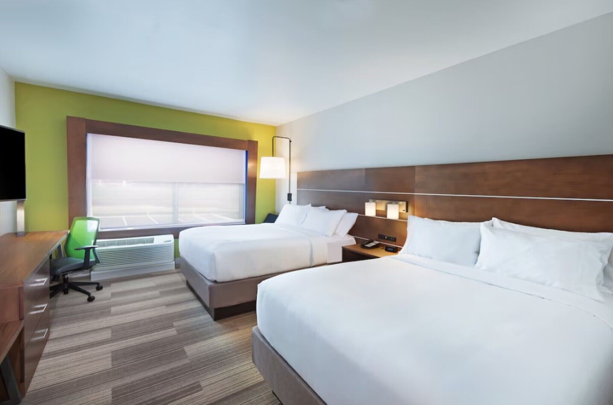 A hotel room with two beds, a desk, a chair, a TV, and a window with blinds.